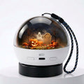 A Halloween-themed portable snow globe speaker with a white body, black base, and a black-and-blue carrying strap. Inside the clear globe, a spooky scene features jack-o'-lanterns, bare trees, a tombstone reading 'R.