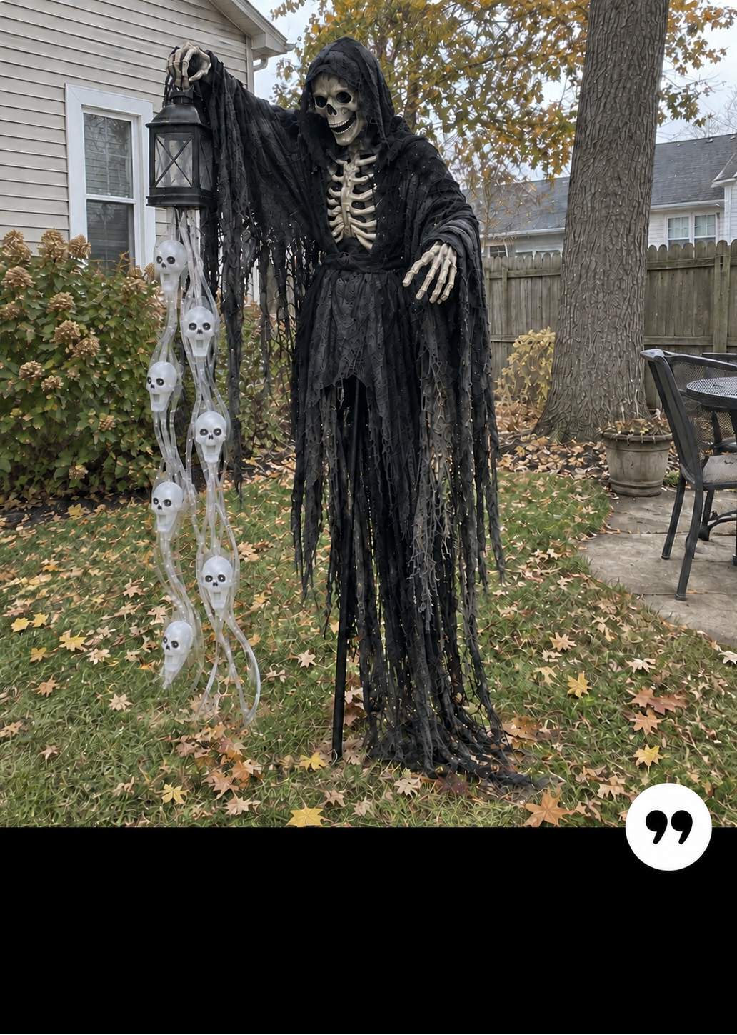A Halloween yard decoration featuring a tall hooded grim reaper figure draped in black fringed fabric, holding a lantern, with a string of hanging skull props on a lawn in front of a house.